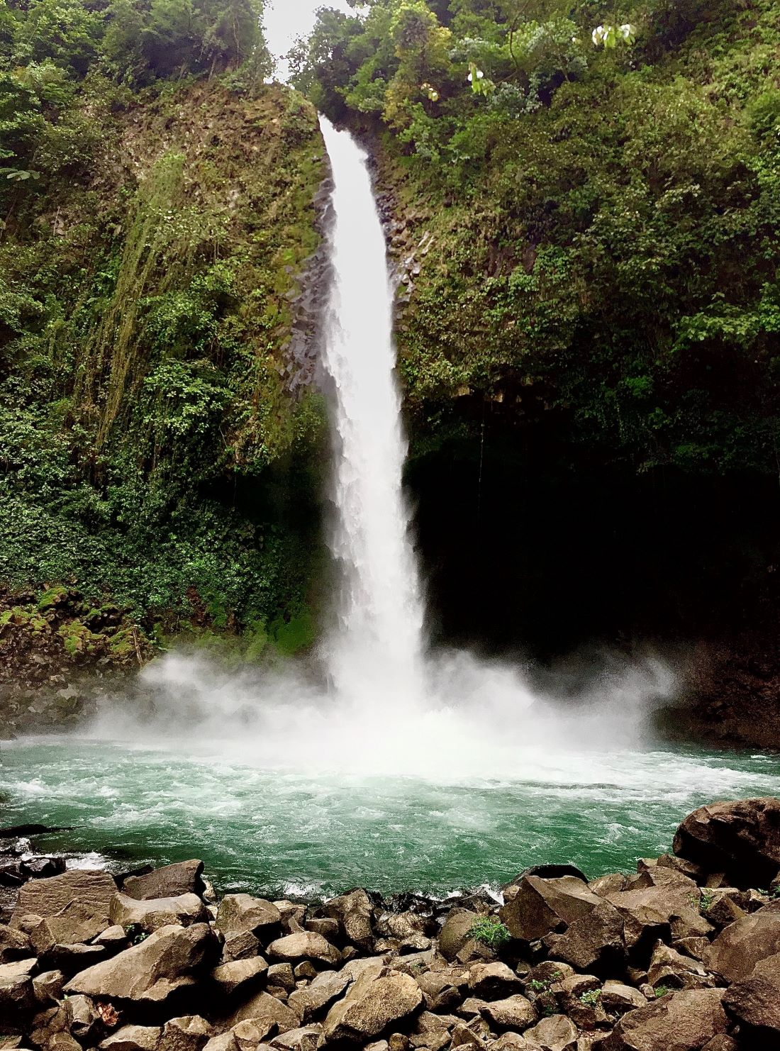 A narrow waterfall hits a small pond with mist rising up from below