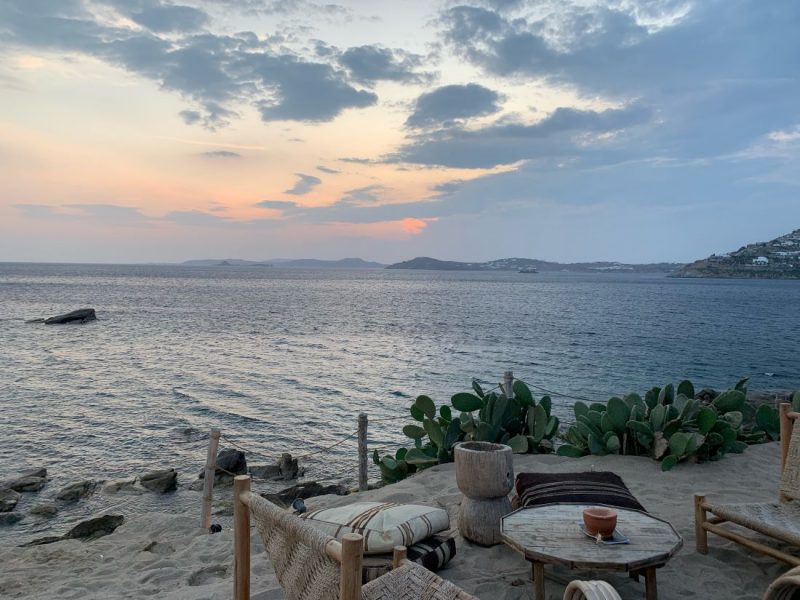 Looking out into sea, from a beach. Wooden furniture, a tables and chairs on the beach.