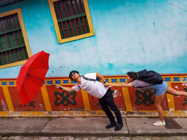 Man holding a red umbrella and a woman's hand, looking like they're being blown away in Guatape