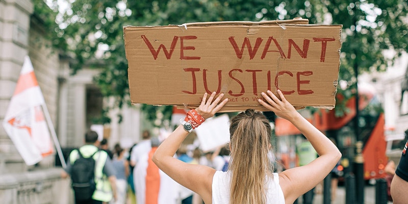 Woman holding a sign that says "We want justice" for a Wanderful event called "Allyship in Action: Creators Holding Travel Brands Accountable"