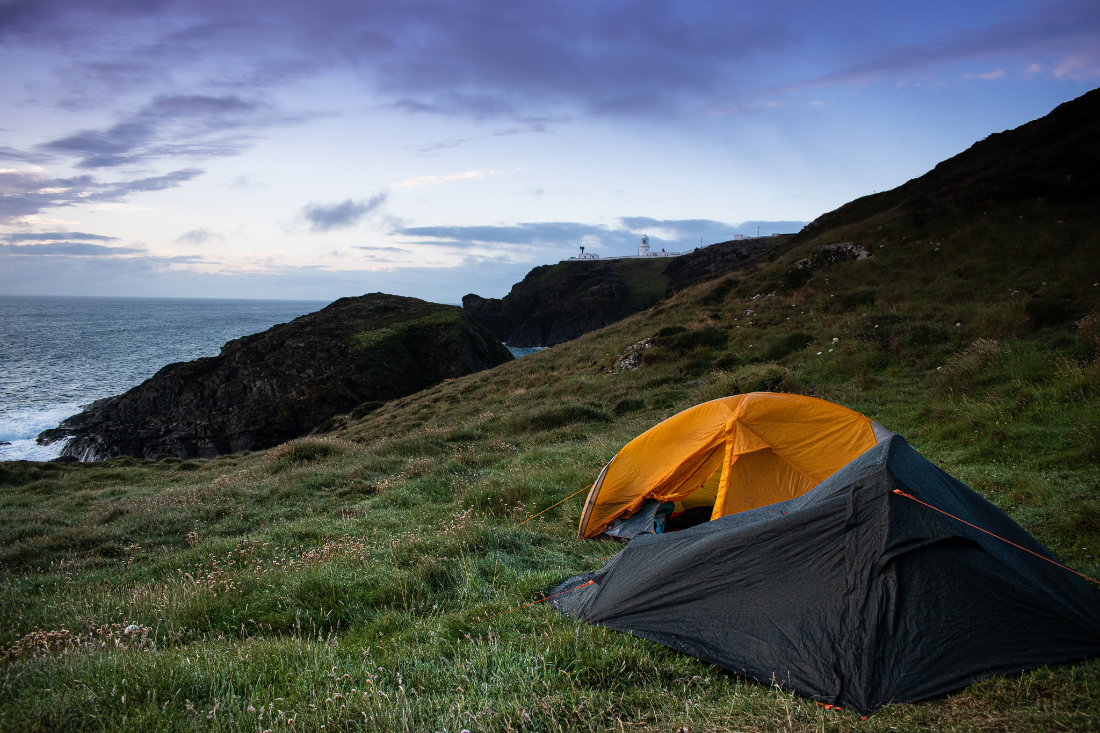 Two small tents set up on a green hillside by the sea